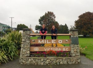Two people standing behind a Mileo, Victoria, BC sign